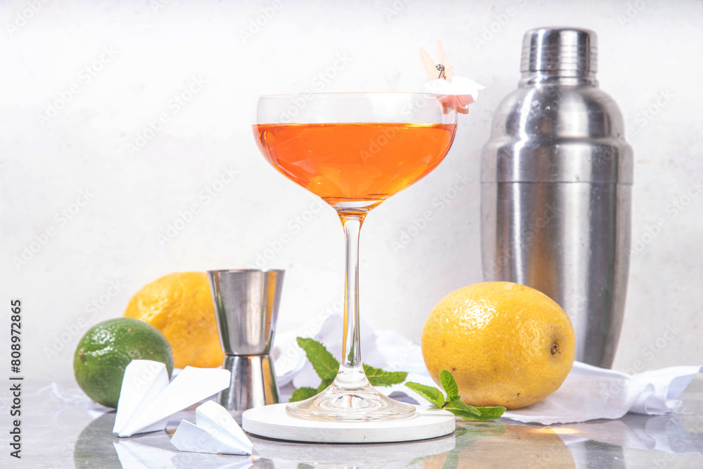 Fototapeta premium Paper plane boozy alcohol cocktail with Bourbon, whiskey, amaro, aperol aperitif, fresh lemon juice and paper plane craft made decor, on white background with hard light and bar utensils