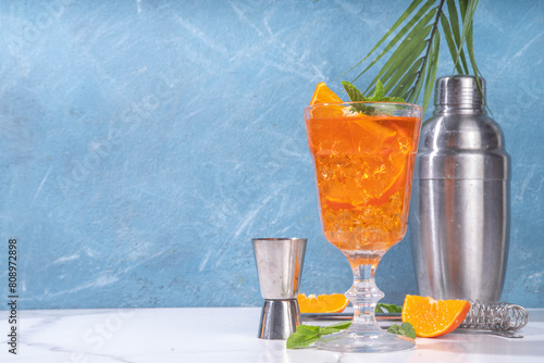 Classic italian aperitif aperol spritz cocktail in glass with ice cubes, alcohol sweet long alcohol drink with slice of orange and mint, on white background with hard light and bar utensils