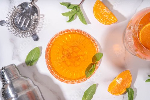 Classic italian aperitif aperol spritz martini cocktail in glass with ice cubes, alcohol sweet long alcohol drink with slice of orange and mint, on white background with hard light and bar utensils