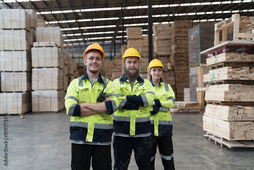 Group of male and female warehouse workers standing together with crossed arms and smiling in industry factory, wearing safety uniform and helmet. Warehouse workers working in warehouse storage