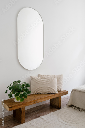 Bedroom with pilea houseplant and cushion on wooden bench under mirror © brizmaker