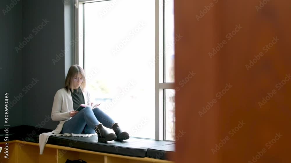 student seated by large window in university library immersed in reading soft natural light quiet atmosphere provide perfect setting for her focused study with touch of warmth from colorful interior student seated by large window in university library immersed in reading soft natural light quiet atmosphere provide perfect setting for her focused study with touch of warmth from colorful interior