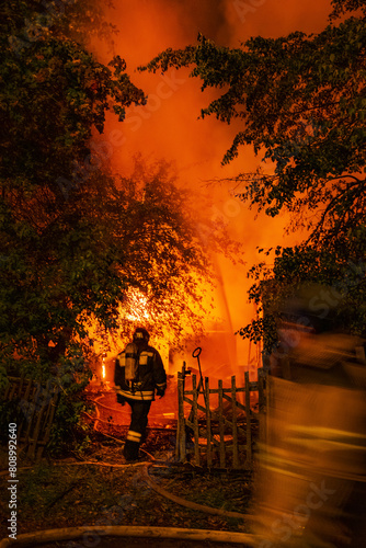 Firefighters silhouette against background of orange glow from fire in country house at night. Fire extinguishing work. Motion blur