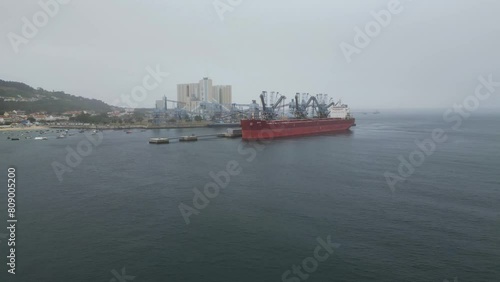 Spectacular drone footage of Trafaria Silopor Harbor captures vibrant maritime activity. Cargo ships unload against the charming coastal town backdrop. Perfect for travel and maritime projects. photo