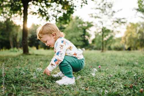 Boy catches soap bubbles in nature. Toddler little cute walking and playing in spring garden. 2 year old boy enjoying on green grass in park on sunny summer day. Outdoors creative activities for kids.