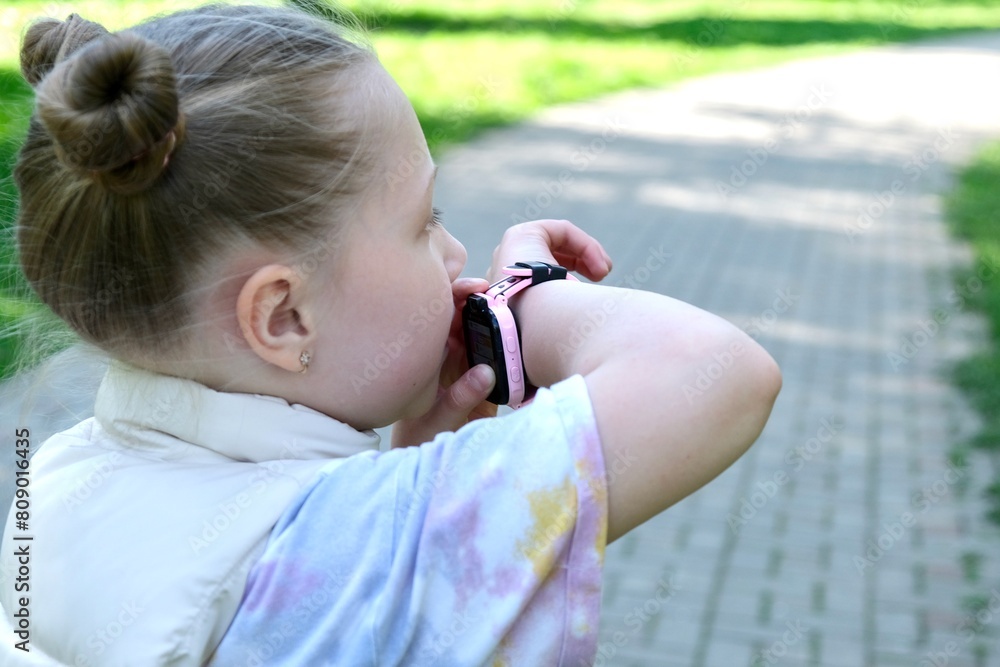 A schoolgirl girl uses a smart watch on a walk in the park. Gadgets, children's smart watches A schoolgirl girl uses a smart watch on a walk in the park. Gadgets, children's smart watches