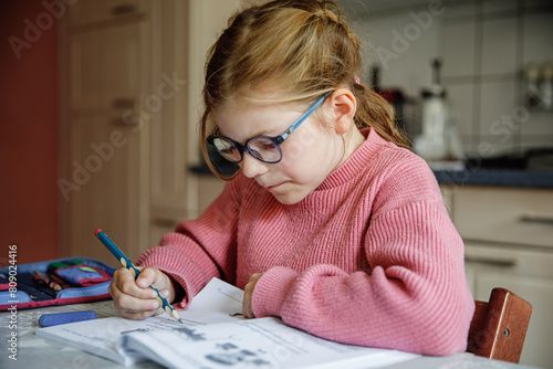 Portrait of happy little girl doing homework at home. Elementary school studing writing and learning. Smiling child writing letters, learing to write. photo