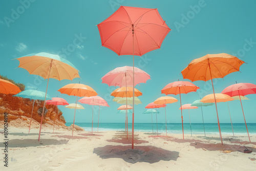 A surreal depiction of oversized  brightly colored umbrellas floating above a deserted sandy beach under a clear blue sky 