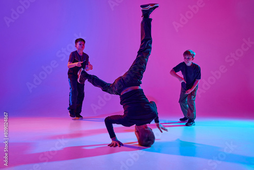Neon dance battle. Dancer performing impressive headstand, breakdance moves in mixed neon light against vibrant gradient background. Concept of sport and hobby, music, fashion and art, movement. Ad