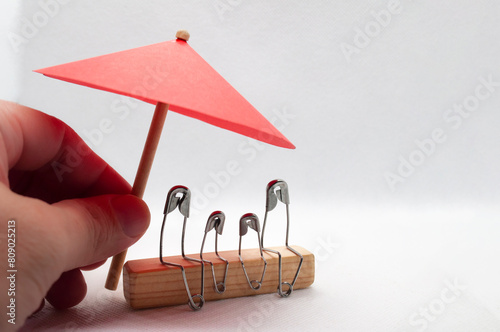 Model safety pin of family sitting on wooden block with red umbrella background. Insurance concept