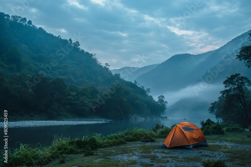 Orange tent by a misty river with lush green mountains in the background,