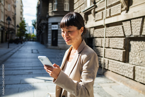 Professional Asian woman using smartphone on sunny city street photo