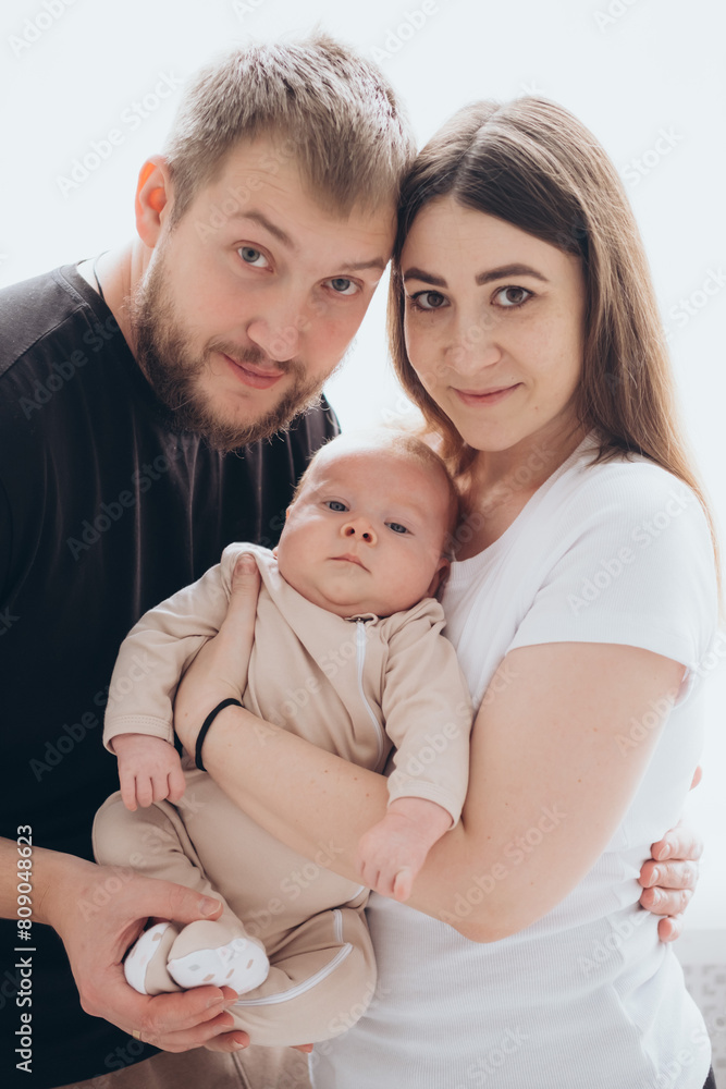 mom and dad with a baby in their arms on a white isolated window background, parents hugging and kissing a newborn baby at home by the window, a happy family mom and dad with a baby in their arms on a white isolated window background, parents hugging and kissing a newborn baby at home by the window, a happy family