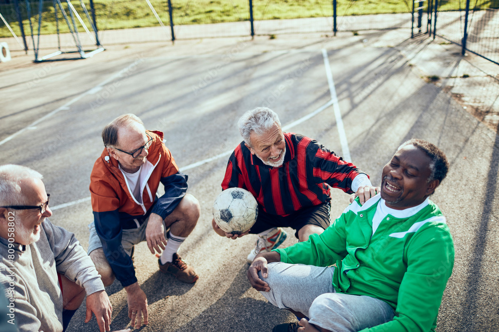 Senior men resting and laughing together after soccer game in park Senior men resting and laughing together after soccer game in park