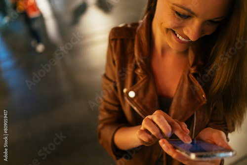 Smiling woman using smartphone at night on city street