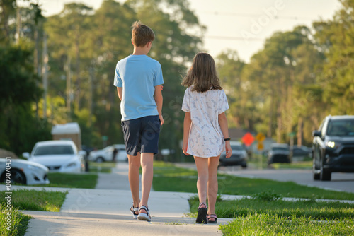 Valokuva Rear view of two young teenage children, girl and boy, brother and sister walking together on rural street on bright sunny day