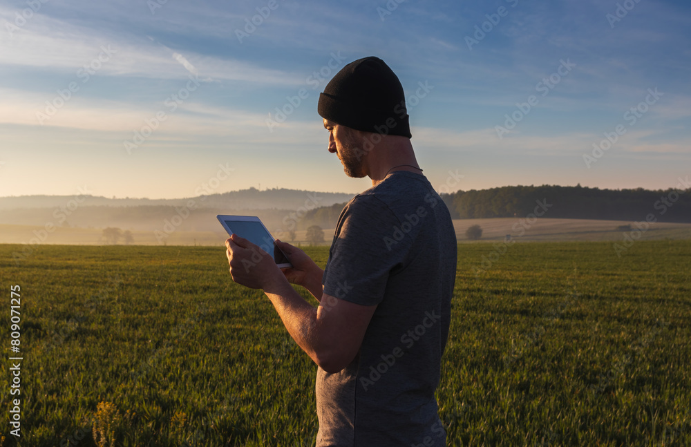 Man, traveler in hat using tablet in spring fog Czech landscape Man, traveler in hat using tablet in spring fog Czech landscape