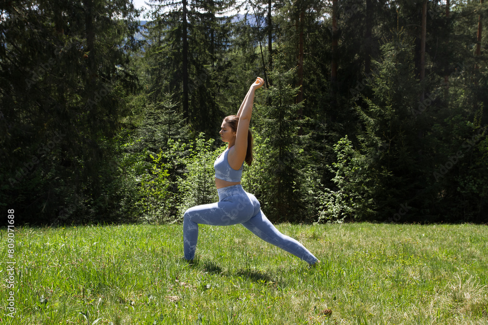 Plus size girl doing physical exercises, sports, yoga, in a blue tight-fitting suit in the fresh air