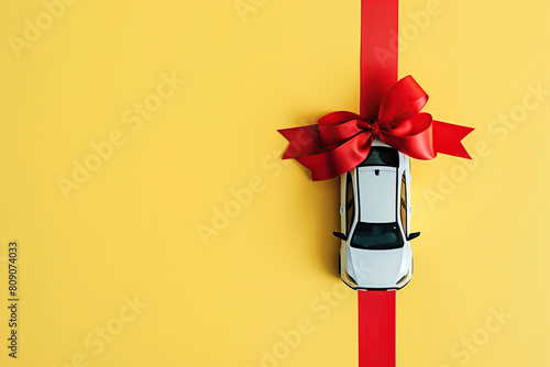 White model car with red ribbon bow on a yellow background. Car as gift, surprise. Present concept. Close up full length size of toy car isolated on color backdrop, copyspace. Rental, auto dealership