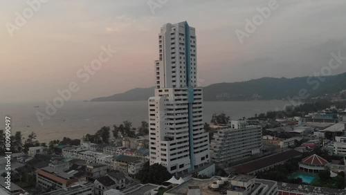 Drone footage of a prominent high-rise tower in Patong, capturing the urban landscape against a backdrop of the ocean and sunset