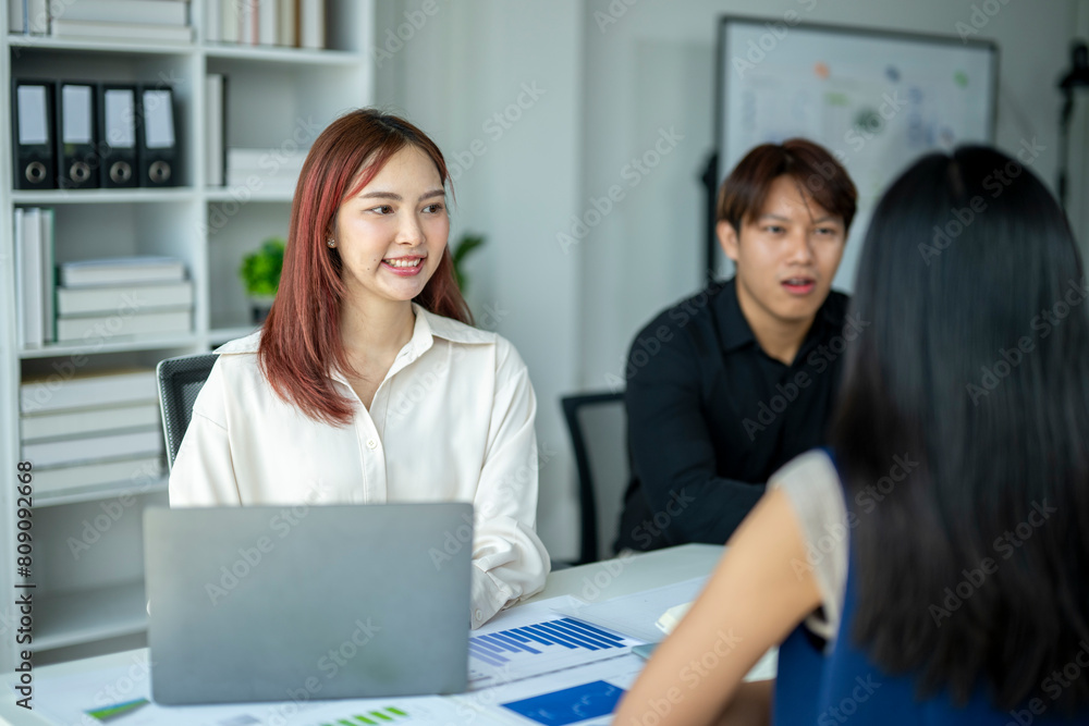 A woman is sitting at a desk with a laptop and a man and woman are talking to her A woman is sitting at a desk with a laptop and a man and woman are talking to her