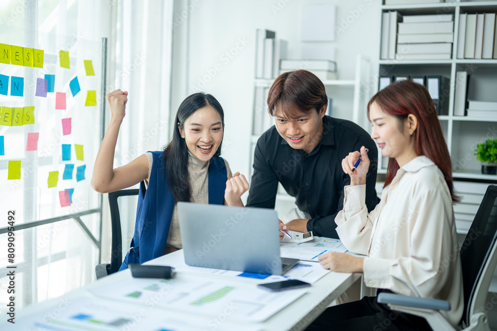 Three people are sitting at a table with a laptop and papers. They are smiling and seem to be happy Three people are sitting at a table with a laptop and papers. They are smiling and seem to be happy