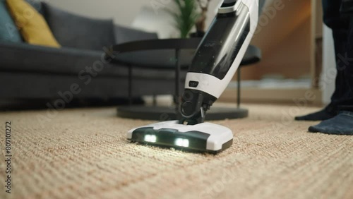 Close up shot - Unrecognisable person vacuuming a jute rug with lights on, on the head of the wireless vacum cleaner
