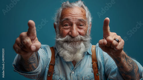 Cheerful elderly man with tattoos pointing towards the camera