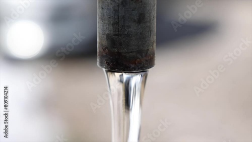 inquadratura ravvicinata e in primo piano di un rubinetto di metallo all'aperto da cui esce dell'acqua fresca e con sfondo sfuocato photo
