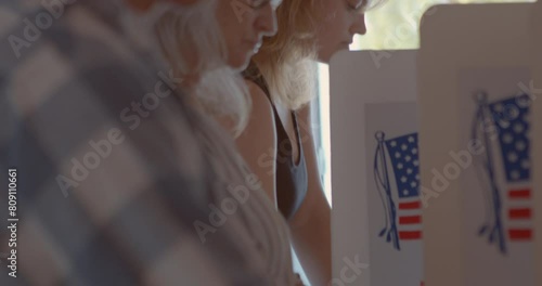 Close up on a diverse group of voters at a polling station concentrating and voting on their political choices with American Flag in the background