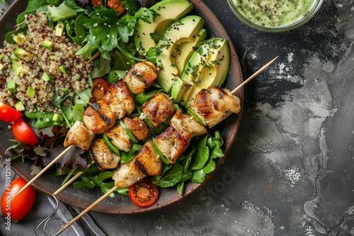 Healthy flat lay of chicken kebabs on a bed of leafy greens, quinoa salad, and sliced avocados