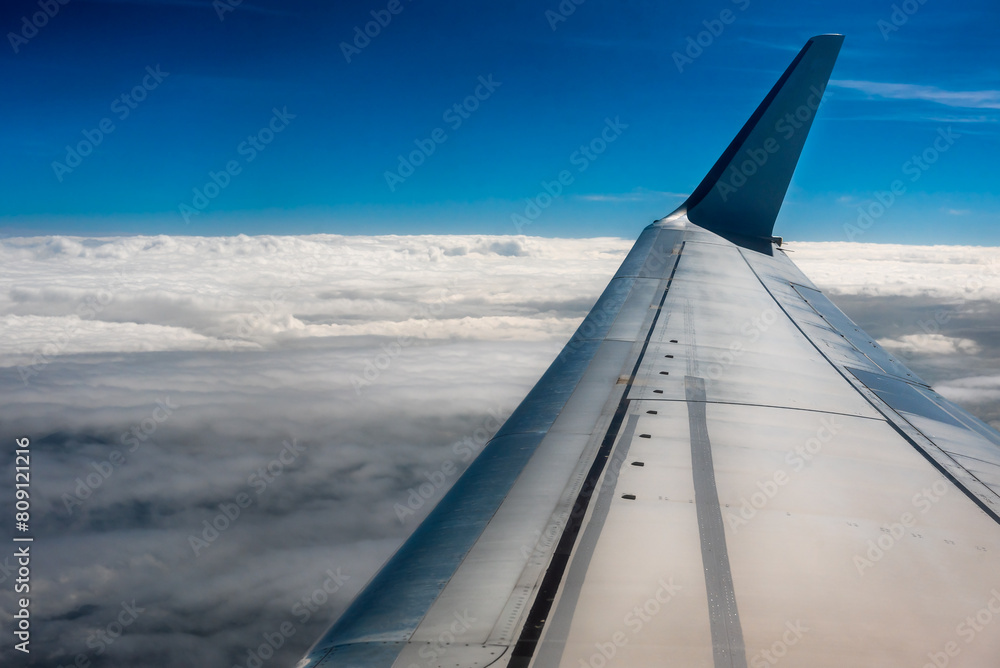 Wing of an airplane above the clouds. The view from the airplane window to the clouds and sunset. Airplane wing above thick white clouds.
