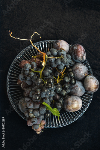 natural dark background with a plate of dark grapes and plums