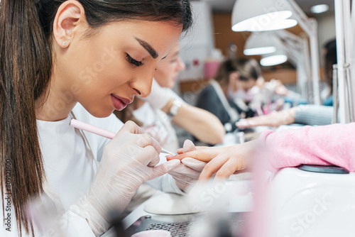 Professional manicurists working in a modern beauty salon. Satisfied female clients receiving nail manicure treatments at spa center.