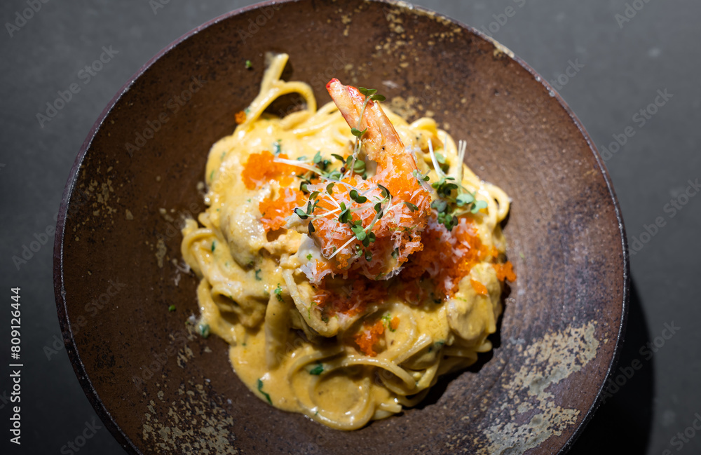 Spaghetti Carbonara pasta Egg and Cheese creamy cream sauce with Shrimp and micro herb decoration on the top of it of earthware circle bowl in studio light. Spaghetti Carbonara pasta Egg and Cheese creamy cream sauce with Shrimp and micro herb decoration on the top of it of earthware circle bowl in studio light.