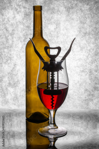 A glass of red wine with a corkscrew inside and a bottle