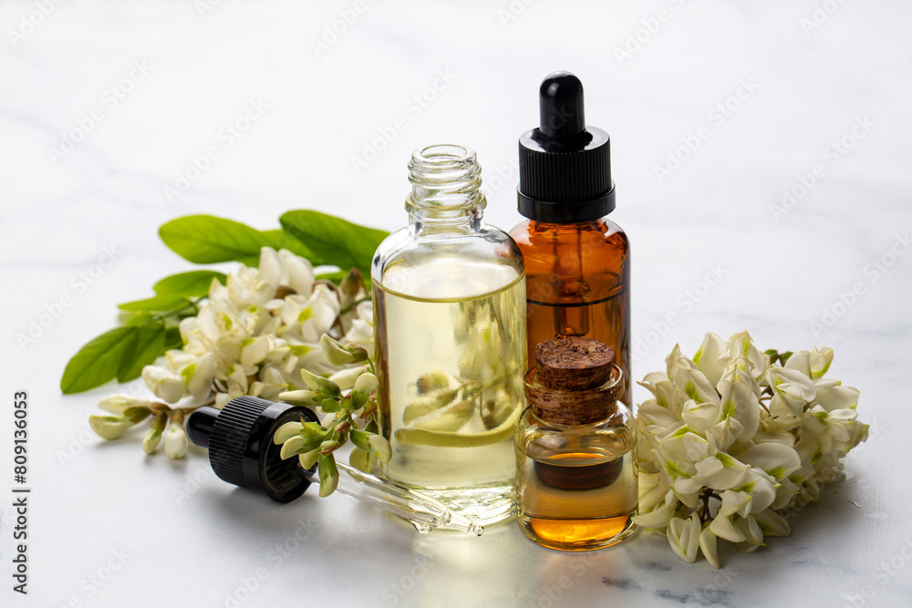 Robinia (false acacia) essential oil (remedy, extract) bottle with fresh acacia flowers Robinia (false acacia) essential oil (remedy, extract) bottle with fresh acacia flowers