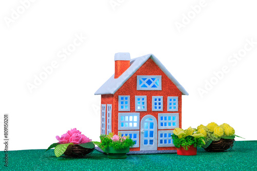 A small red house with blue light in the windows surrounded by flowers