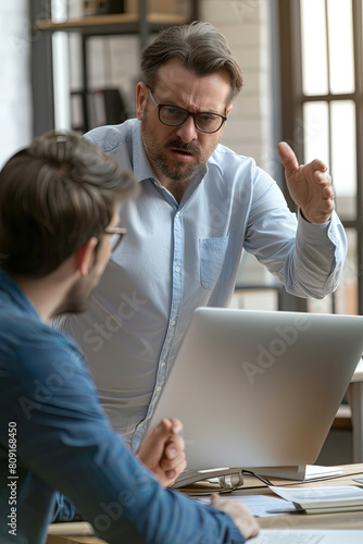 Angry boss criticizing scolding sad male employee for computer mistake incompetence at workplace, mad leader reprimanding rebuking shouting at subordinate lazy worker blaming of bad work in office
 photo