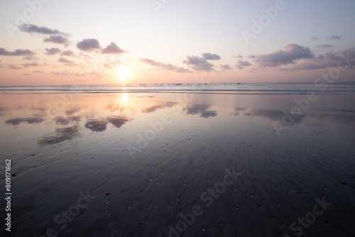 Fantastic sunset on the dream beach of Kuta  small waves setting over the sea and the reflection of the sky in the shallow water. News Bali in Indonesia