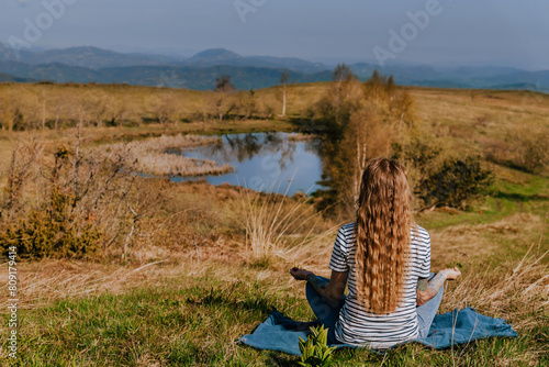 Woman Meditating Sitting Alone near Mountain Lake (ID: 809179414)