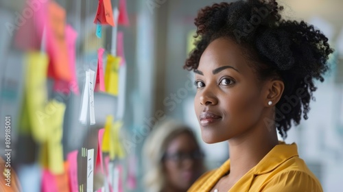 African American woman with colorful sticky notes on glass wall. Creative brainstorming in modern workplace.