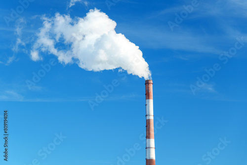 Smokestack emits thick smoke from a pipe, contrasting against a clear blue sky