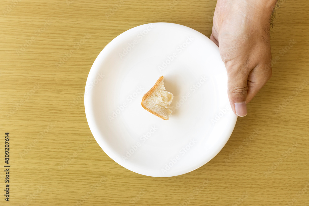 皿にのせた少しのパンを持つ男性の手。貧困のイメージ 皿にのせた少しのパンを持つ男性の手。貧困のイメージ