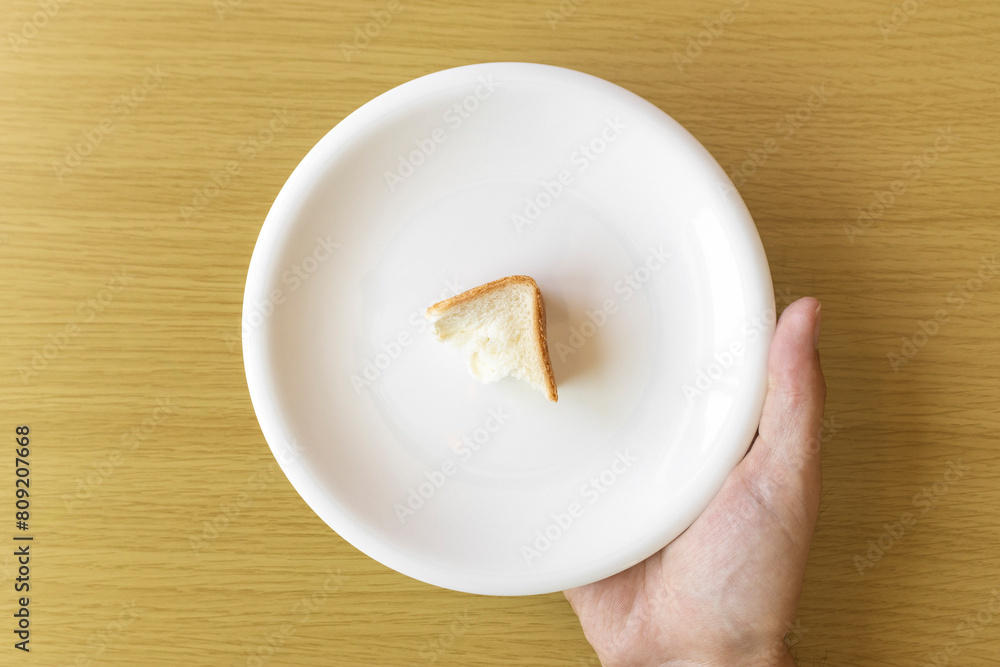 皿にのせた少しのパンを持つ男性の手。貧困のイメージ 皿にのせた少しのパンを持つ男性の手。貧困のイメージ