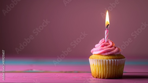   A cupcake topped with pink frosting and a single lit candle embedded within it photo