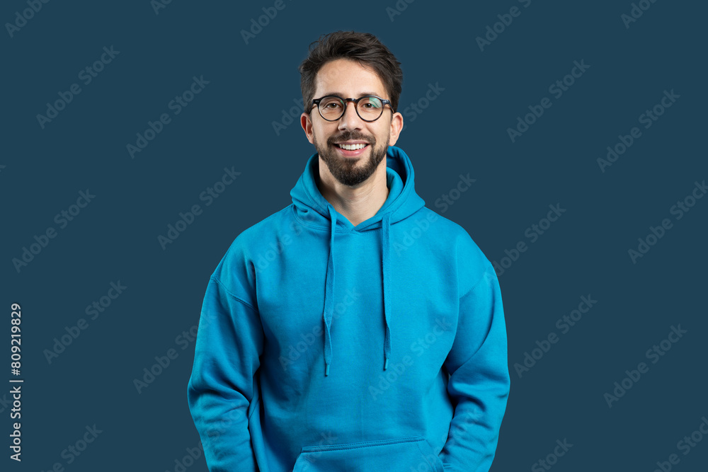 Fototapeta premium A man with a blue hoodie and glasses is standing in the image. He appears to be looking straight ahead. The focus is on his attire and facial features.
