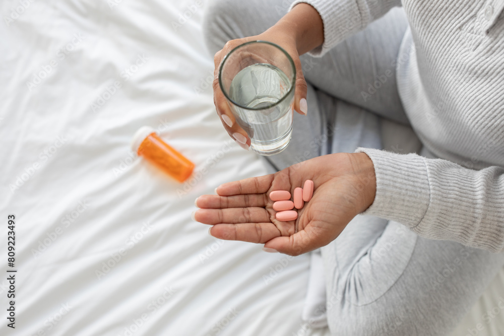 A woman holding a glass of water and a handful of pills in her hand. She appears to be taking medication according to the prescribed dosage, cropped A woman holding a glass of water and a handful of pills in her hand. She appears to be taking medication according to the prescribed dosage, cropped