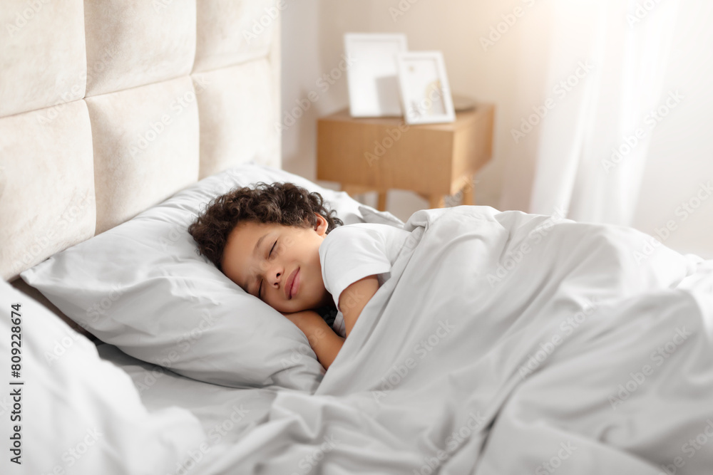 A young African American boy, in pajamas, peacefully sleeps in a cozy bed covered with a white comforter. The room is dimly lit, and the child is curled up comfortably, resting peacefully. A young African American boy, in pajamas, peacefully sleeps in a cozy bed covered with a white comforter. The room is dimly lit, and the child is curled up comfortably, resting peacefully.