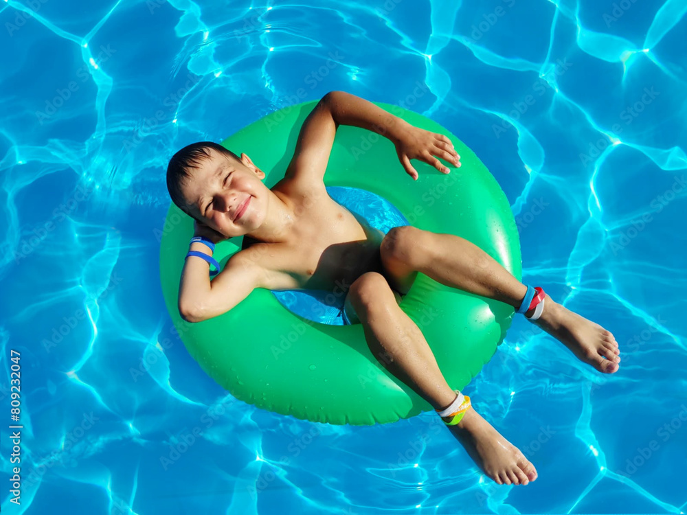 Cheerful happy six-year-old boy in a swimming circle swims in the pool under the sun. Summer holiday